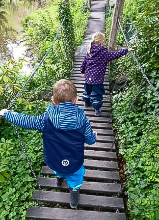 Kinder laufen in Regenkleidung über eine Brücke