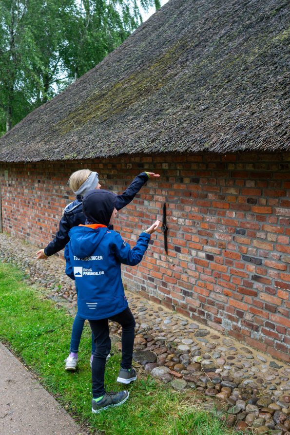 Kinder fangen Regentropfen die von einem Reetdach fallen auf Föhr.