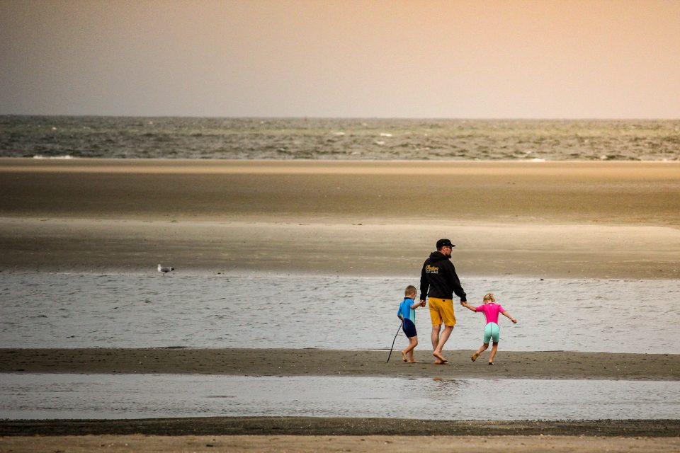 Vater geht mit Kindern am Strand beim Familienurlaub Deutschland mit Kindern