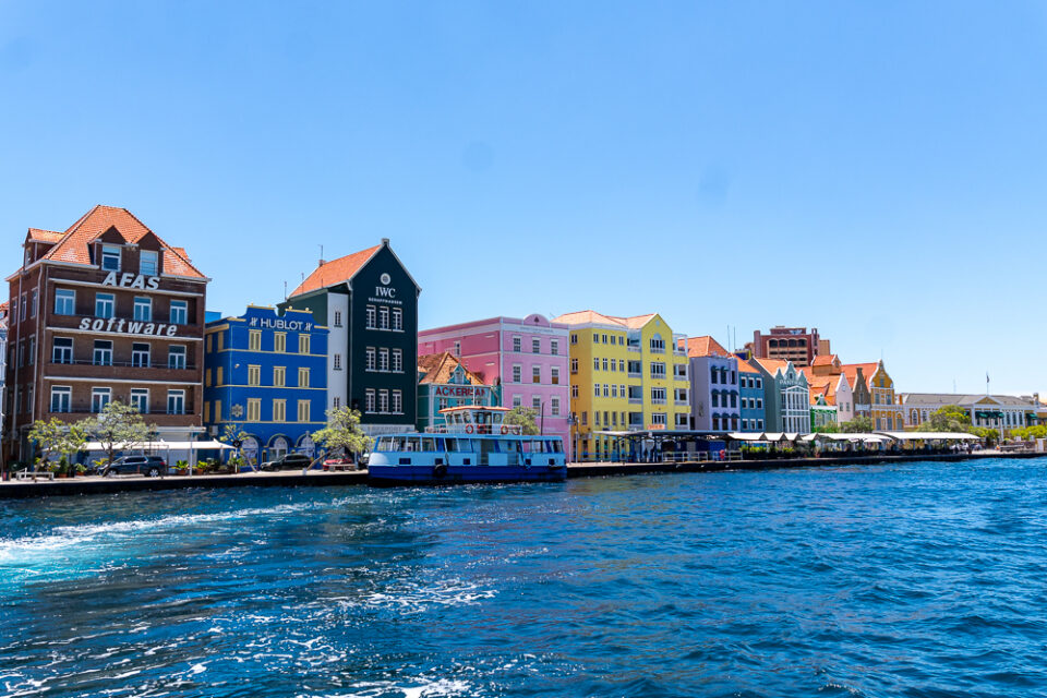 Bunte Kolonialhäuser an der Uferpromenade von Willemstad auf Curaçao mit türkisblauem Meer im Vordergrund